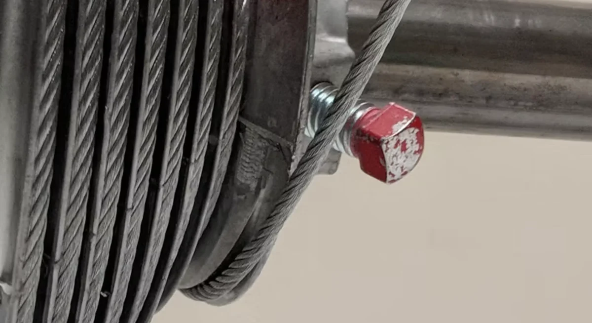 Close-up of a garage door cable drum with the lift cable wound around it, next to the torsion shaft and its set screw